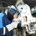 professional repairman worker in automotive industry welding metal body car with sparks